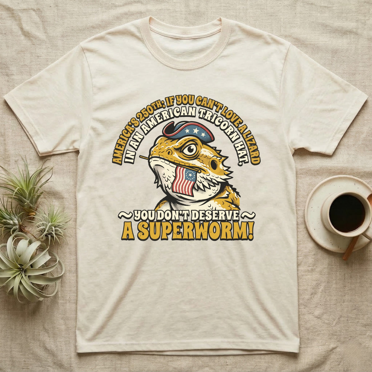 Bearded Dragon Tricorn Tee in Natural — Bold woodcut tee of a bearded dragon in a colonial tricorn hat, gold and cream text reading You Don't Deserve A Superworm, on black.