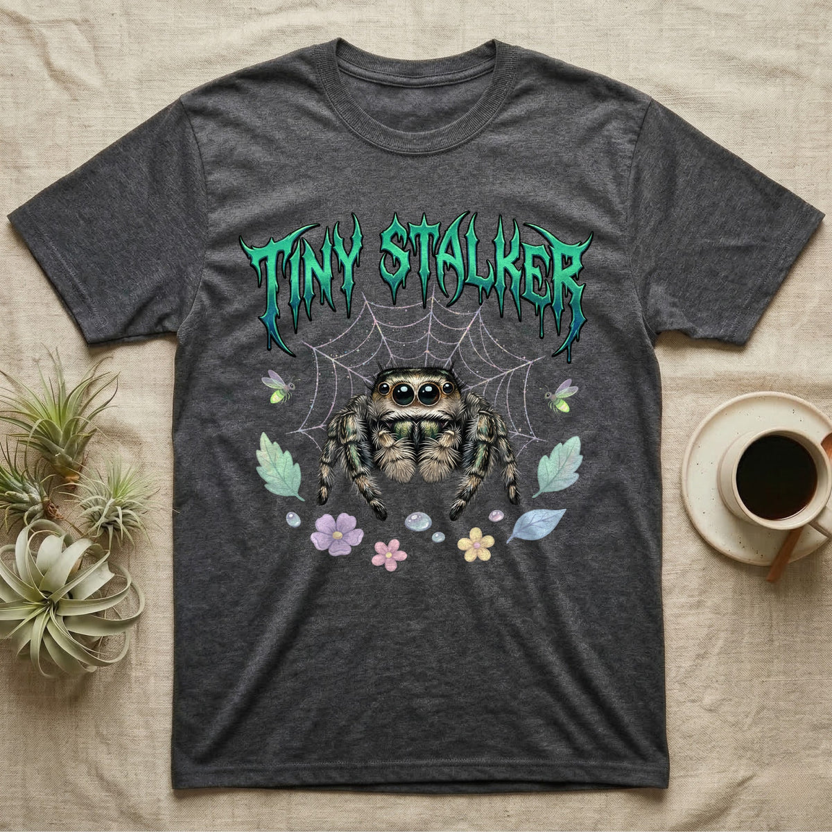 Regal Jumping Spider Feral T-Shirt in Dark Heather — Fuzzy jumping spider with huge eyes in a pastel garden under a spiky iridescent-teal metal wordmark reading TINY STALKER.
