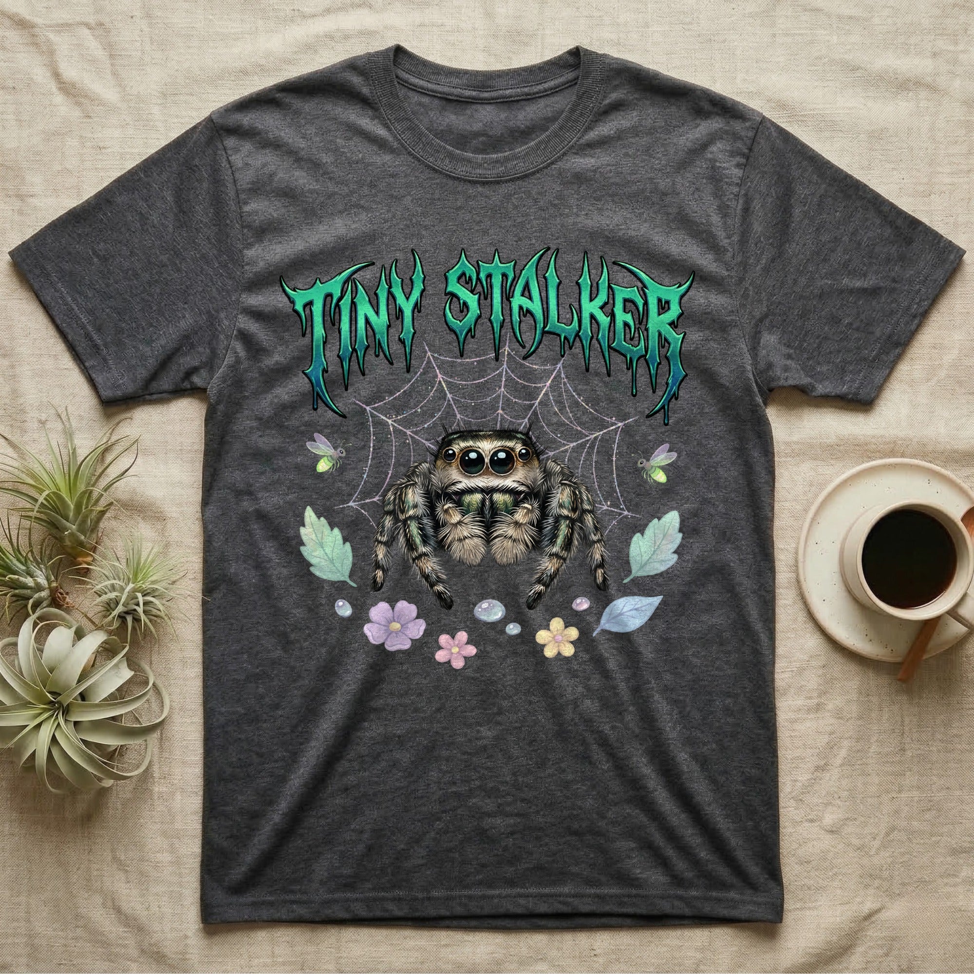 Regal Jumping Spider Feral T-Shirt in Dark Heather — Fuzzy jumping spider with huge eyes in a pastel garden under a spiky iridescent-teal metal wordmark reading TINY STALKER.