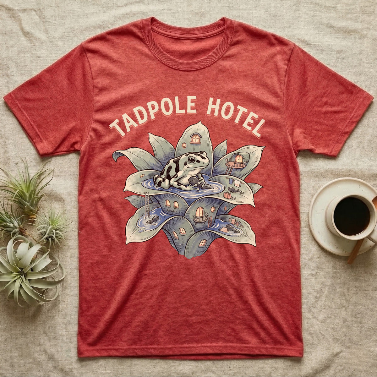 Tadpole Hotel Frog T-Shirt in Heather Red — Whimsical naturalist illustration of a dart frog tucking tadpoles into a bromeliad Tadpole Hotel with hand-lettered marquee text.