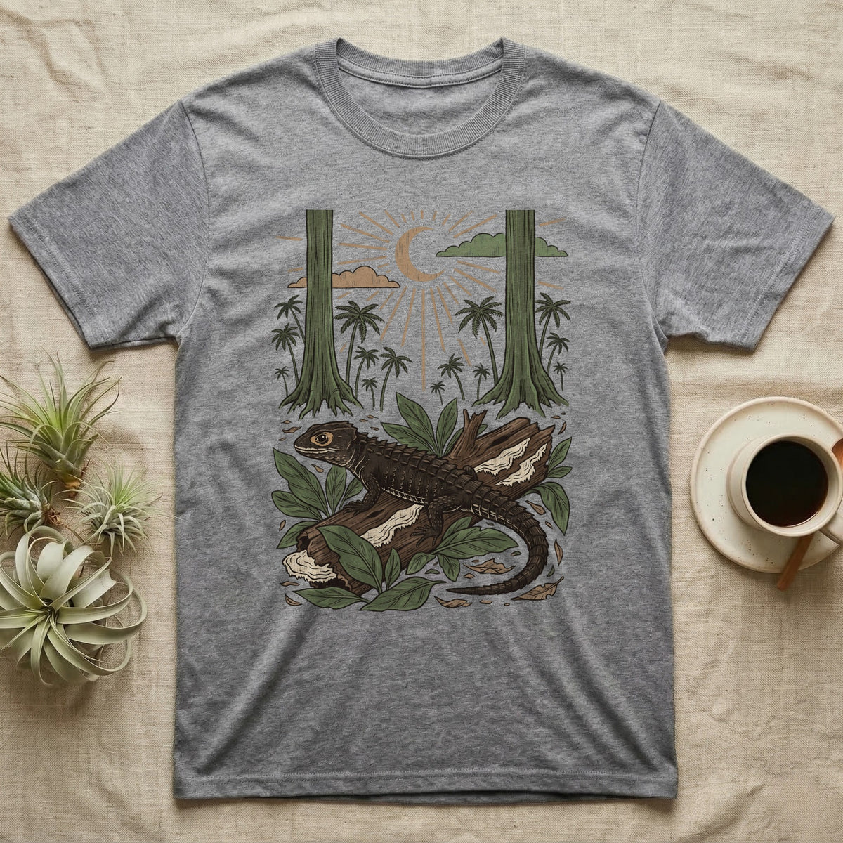 Crocodile Skink Home Range T-Shirt in Sport Grey — Woodcut-style illustration of a red-eyed crocodile skink crouched on a rainforest log among broad leaves and palms, no on-shirt text.