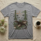 Crocodile Skink Home Range T-Shirt in Sport Grey — Woodcut-style illustration of a red-eyed crocodile skink crouched on a rainforest log among broad leaves and palms, no on-shirt text.