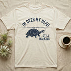 Musk Turtle Walking T-Shirt in Natural — Navy silhouette of a musk turtle walking under arched words In Over My Head, beside Still Walking