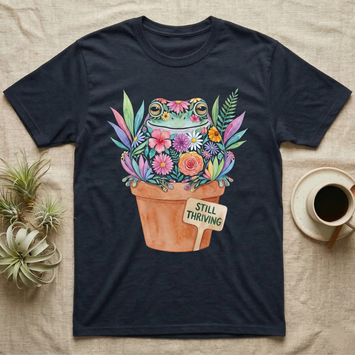 Tree Frog Thriving T-Shirt in Navy — A White's tree frog made of watercolour flowers, sitting in a terracotta pot with a plant label reading STILL THRIVING.