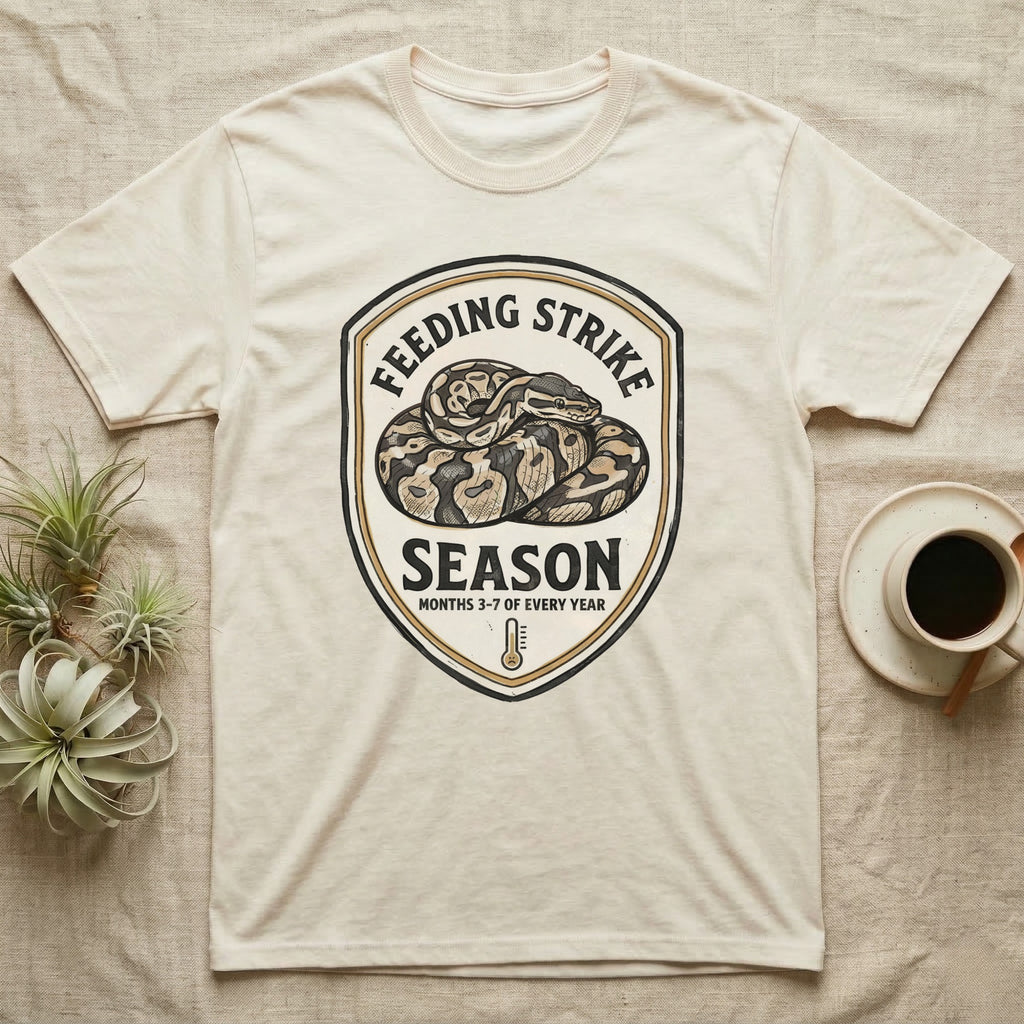 Ball Python Feeding Strike T-Shirt in Natural — Vintage-ink badge of a coiled ball python with carved type "Feeding Strike Season" and fine print "Months 3-7 Of Every Year."