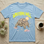 Sulcata Tortoise Feral T-Shirt in Light Blue — Sulcata tortoise plodding over crumbled bricks under a jagged caution-yellow metal "WRECKING BALL" wordmark.