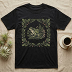 Black t-shirt with a central illustration of a frog in a forest scene with ferns and mushrooms.