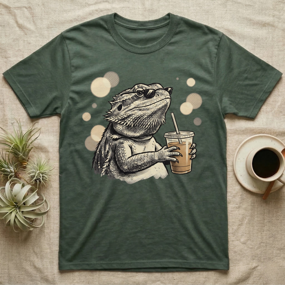 Cold Brew Bearded Dragon T-Shirt in Military Green — Flat near-photoreal illustration of a bearded dragon in tiny sunglasses holding a cold brew with warm bokeh.