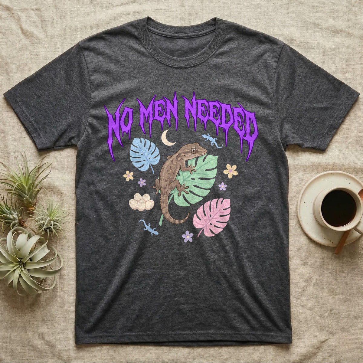 Mourning Gecko Feral T-Shirt in Dark Heather — Mourning gecko on a leaf flanked by clone silhouettes under a jagged violet metal "NO MEN NEEDED" wordmark.