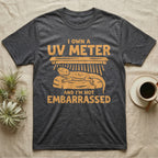 Reptile Keeper UV Meter T-Shirt in Dark Heather — Linocut block-print badge of a UVB tube lamp above an empty basking rock, ringed by carved slogan lettering.