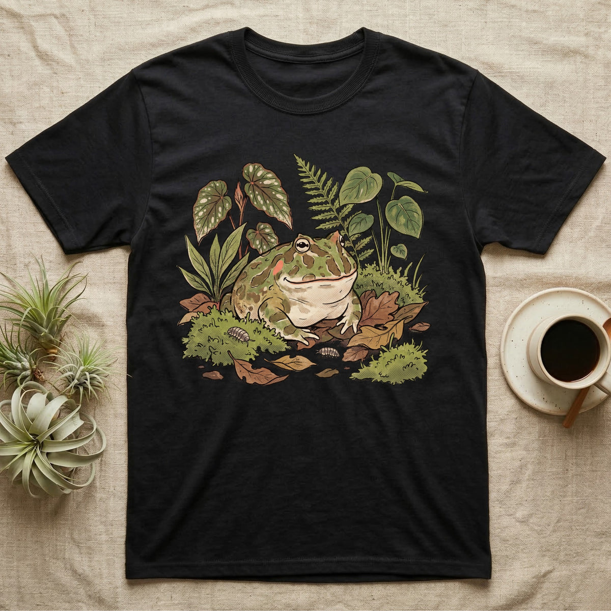 Bioactive Pacman Frog T-Shirt in Black — Warm botanical illustration of a content pacman frog half-buried in a lush bioactive habitat of moss and leaf litter.