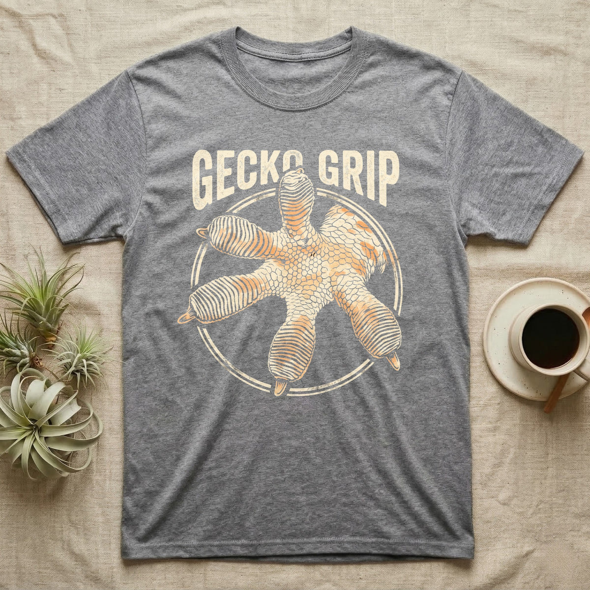 Macro badge illustration of a gecko's splayed foot with ribbed adhesive toe pads inside a distressed circular border, arched wordmark reading GECKO GRIP. — shown on a Sport Grey tee.