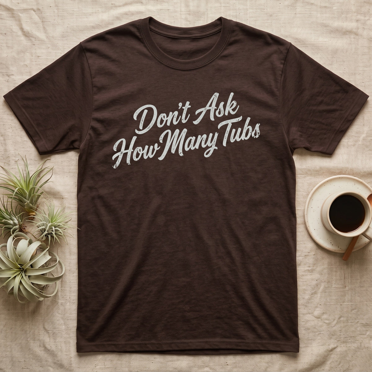 Snake Tubs T-Shirt in Dark Chocolate — Worn off-white 1970s retro brush script climbing a diagonal on charcoal, reading Don't Ask How Many Tubs