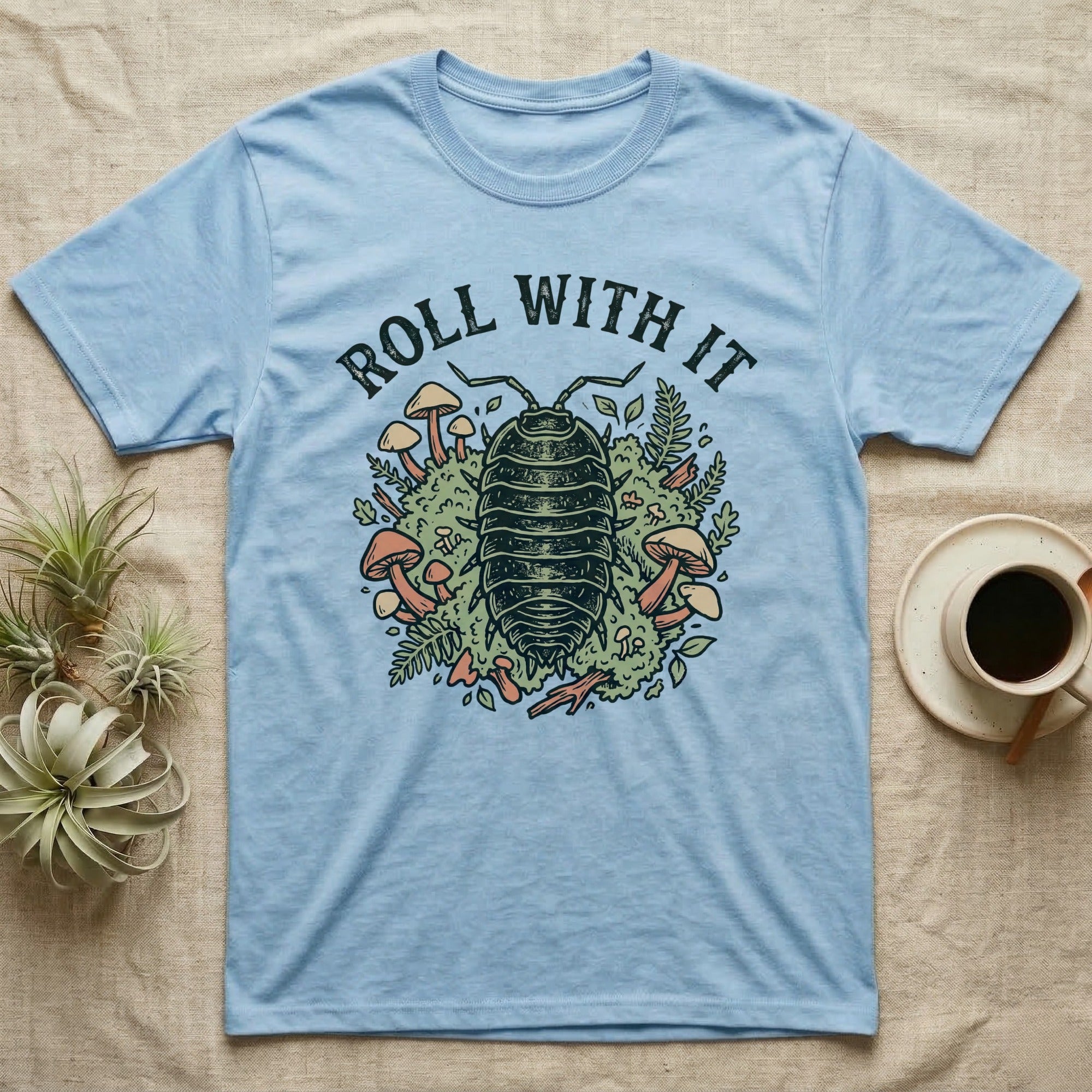 Light blue t-shirt with "Roll With It" text above an illustrated rolly polly and mushrooms.