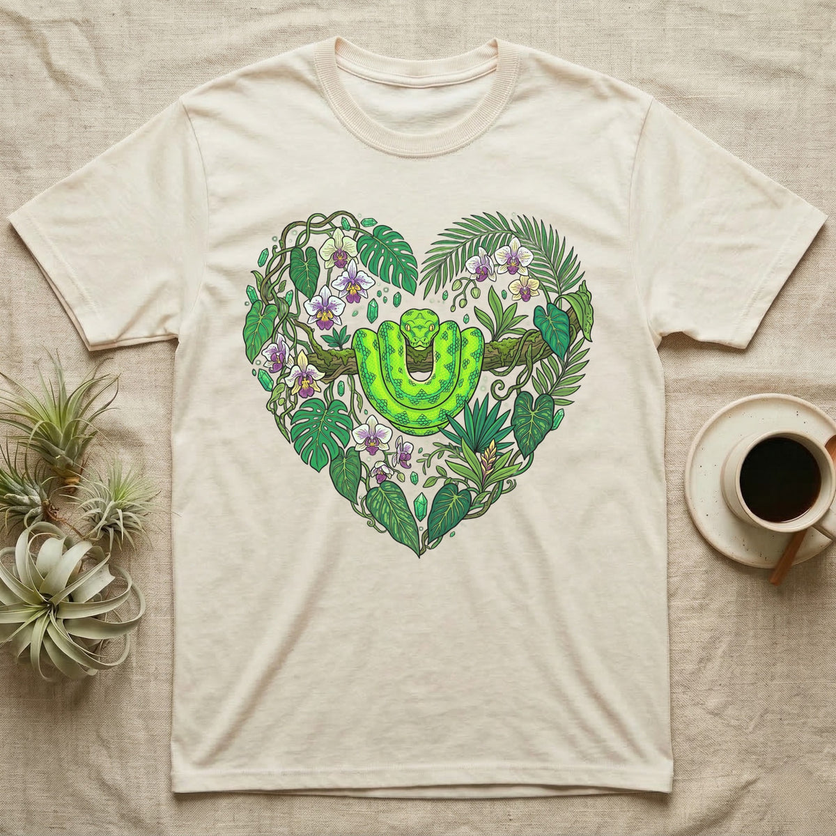 Green snake and tropical leaves form a heart shape on a cream t-shirt.