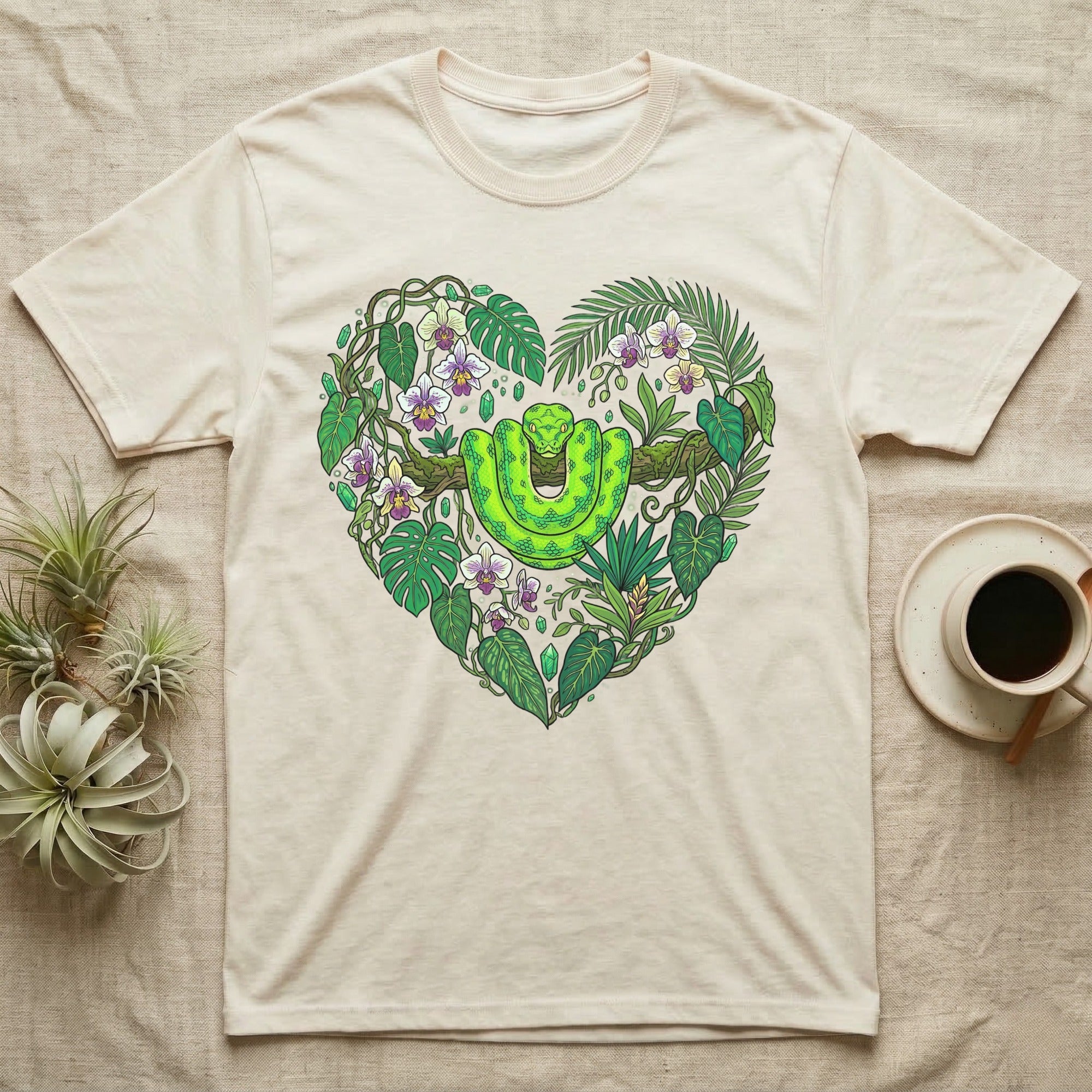 Green snake and tropical leaves form a heart shape on a cream t-shirt.