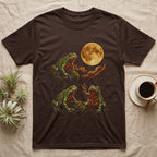 Fire-Bellied Toad Moon T-Shirt in Dark Chocolate — Three fire-bellied toads under a glowing amber full moon, one on a mossy ledge, one reaching a front foot up at the moon