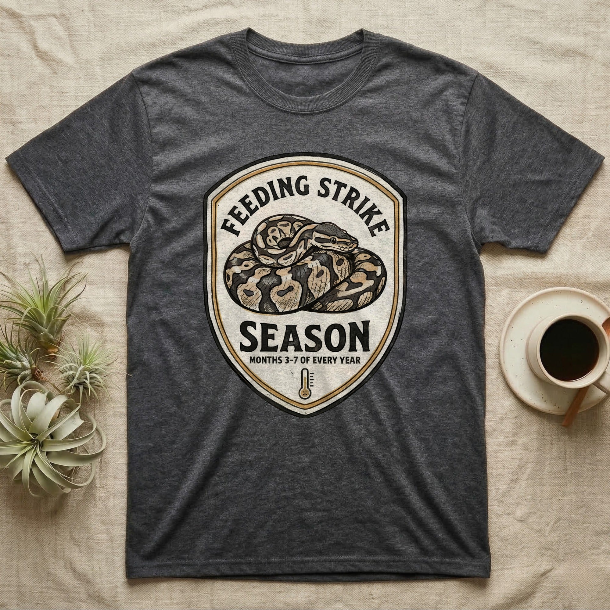 Ball Python Feeding Strike T-Shirt in Dark Heather — Vintage-ink badge of a coiled ball python with carved type "Feeding Strike Season" and fine print "Months 3-7 Of Every Year."