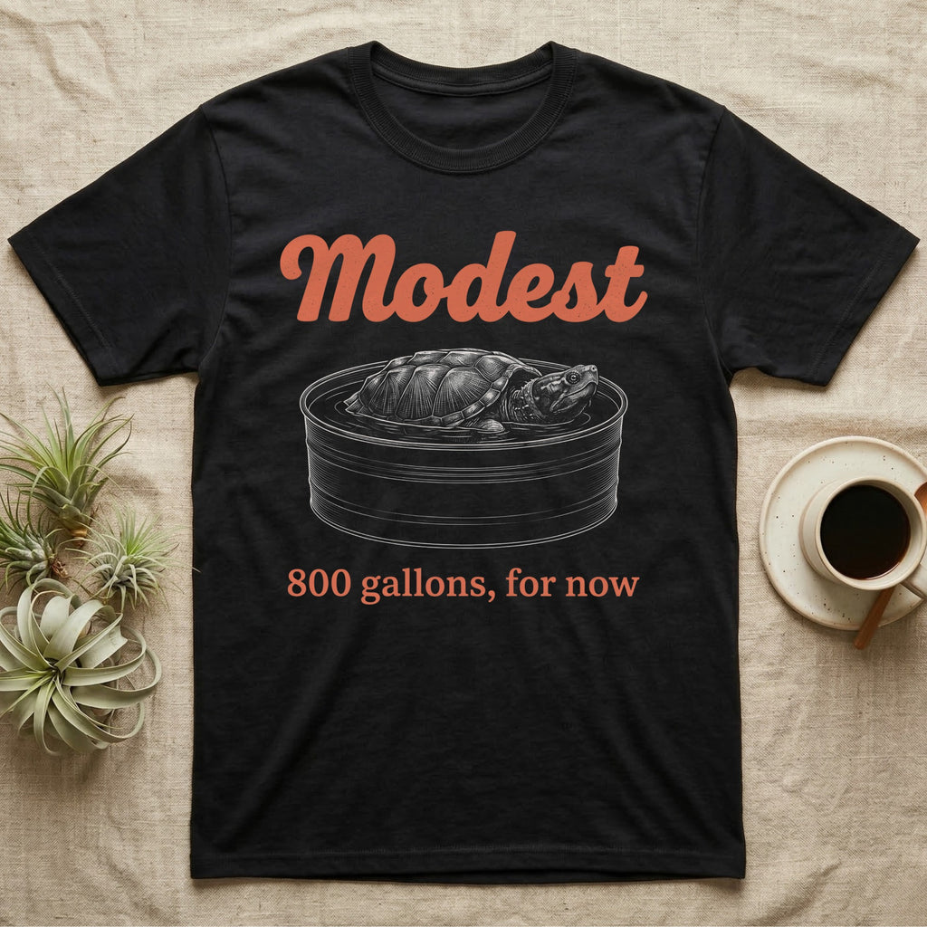 Snapping Turtle Modest T-Shirt in Black — White-line engraving of a huge snapping turtle in a stock tank under orange Modest script and a serif line