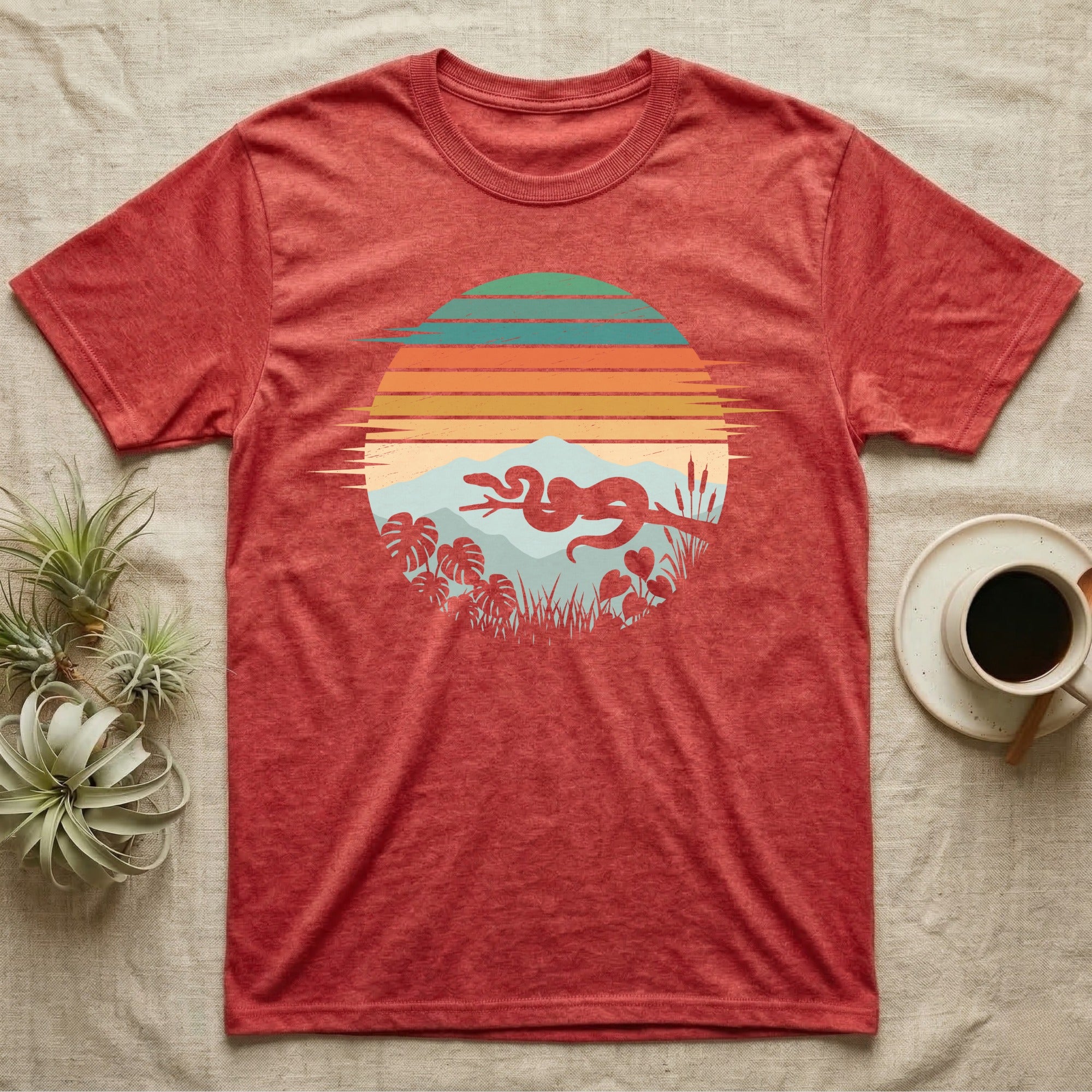Ball Python Retro Sunset T-Shirt in Heather Red — Ball python silhouette draped over a branch inside a retro striped sunset disc with monstera leaves on a tee