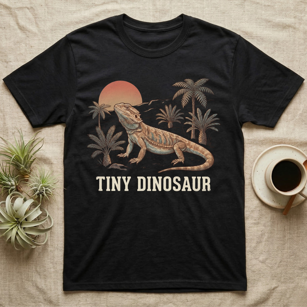Tiny Dinosaur Bearded Dragon T-Shirt in Black — Retro natural-history illustration of a bearded dragon in profile in a prehistoric landscape with a distressed "Tiny Dinosaur" caption.