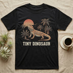 Tiny Dinosaur Bearded Dragon T-Shirt in Black — Retro natural-history illustration of a bearded dragon in profile in a prehistoric landscape with a distressed "Tiny Dinosaur" caption.