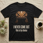 Deadpan photographic mugshot of an African fat-tailed gecko half in shadow above the distressed text I Never Come Out, this is by choice. — shown on a Black tee.