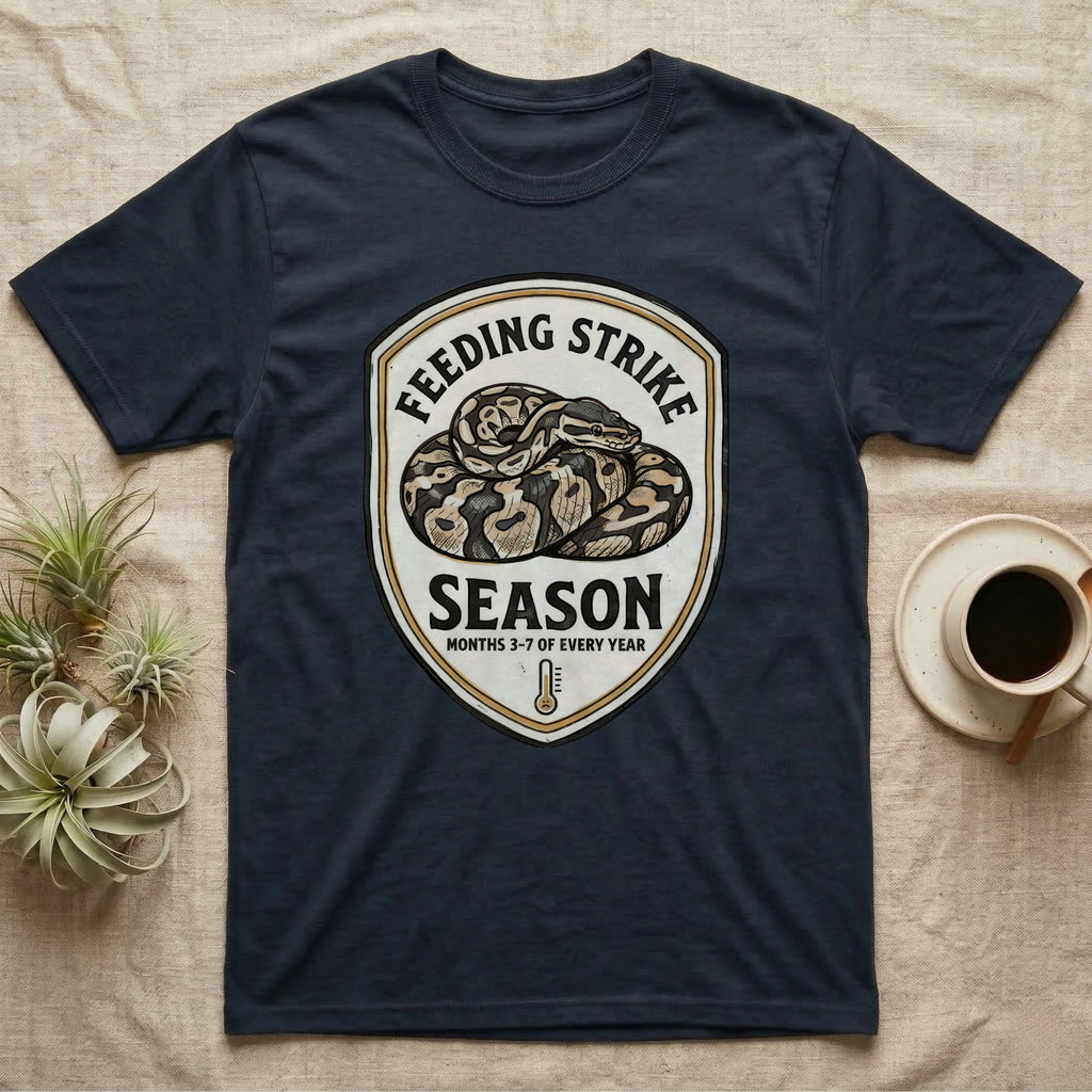Ball Python Feeding Strike T-Shirt in Navy — Vintage-ink badge of a coiled ball python with carved type "Feeding Strike Season" and fine print "Months 3-7 Of Every Year."