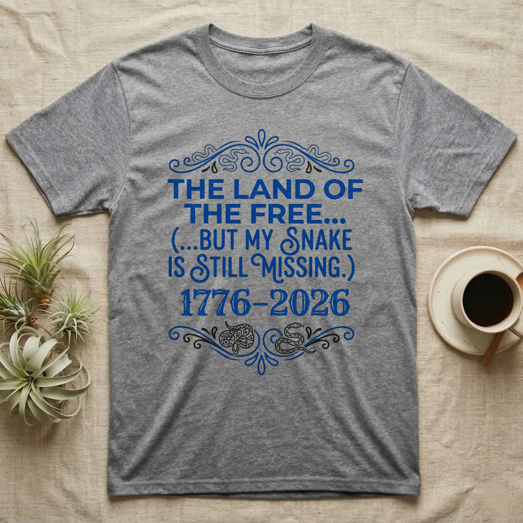Corn Snake Still Missing Tee in Sport Grey — Royal blue typographic tee reading The land of the free but my snake is still missing, with Victorian filigree and small coiled corn snakes.