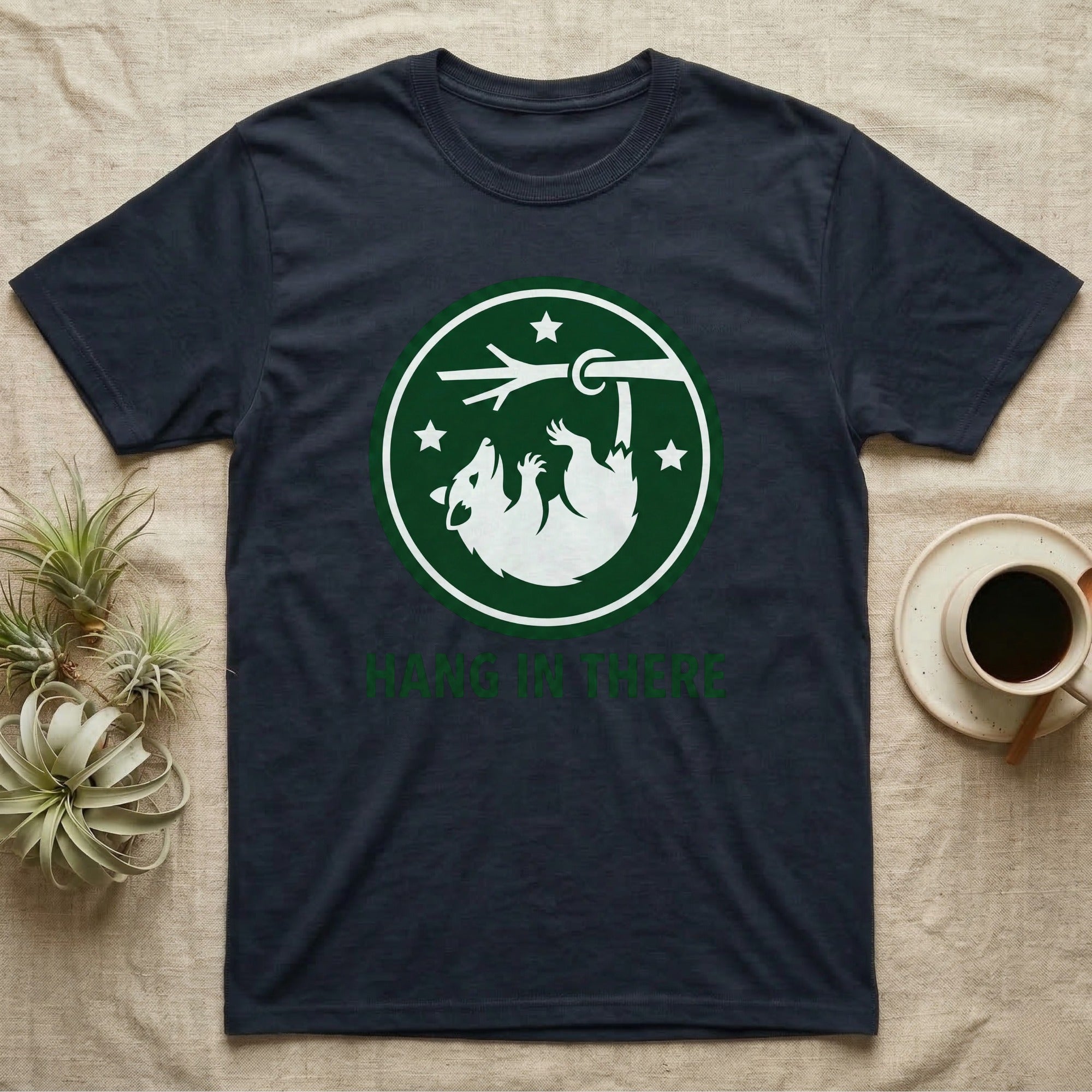 Navy t-shirt with a green circle logo of a raccoon hanging from a branch, text "HANG IN THERE".