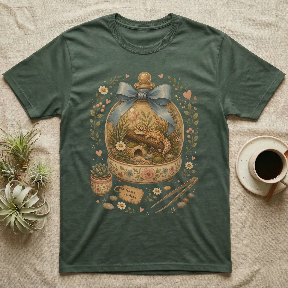 Green t-shirt with a watercolor illustration of a gecko in a terrarium with floral accents.