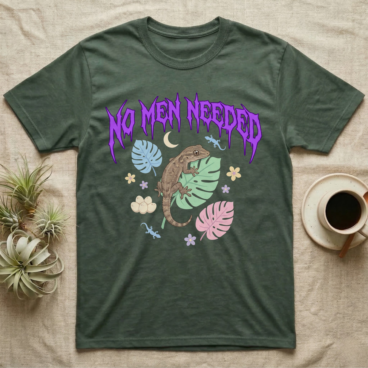 Mourning Gecko Feral T-Shirt in Military Green — Mourning gecko on a leaf flanked by clone silhouettes under a jagged violet metal "NO MEN NEEDED" wordmark.