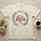 Sulcata Tortoise Salad Love T-Shirt in Natural — Sepia watercolour illustration of a Sulcata tortoise mid-bite inside a salad-greens wreath with "SALAD" lettering.