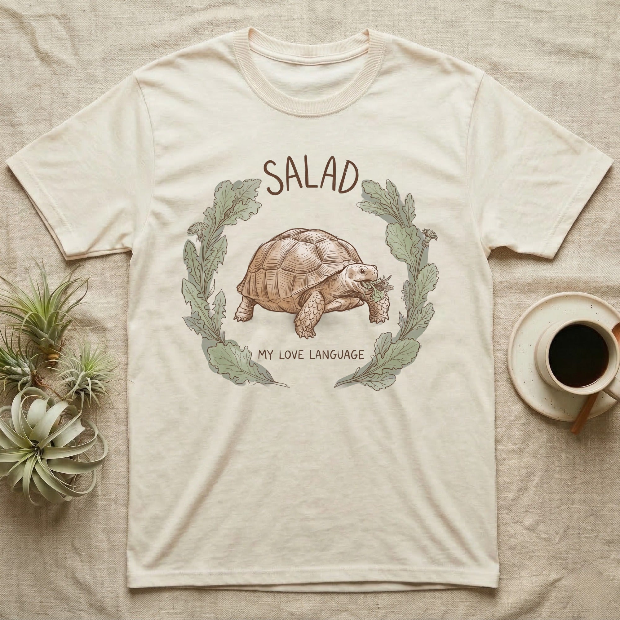 Sulcata Tortoise Salad Love T-Shirt in Natural — Sepia watercolour illustration of a Sulcata tortoise mid-bite inside a salad-greens wreath with "SALAD" lettering.
