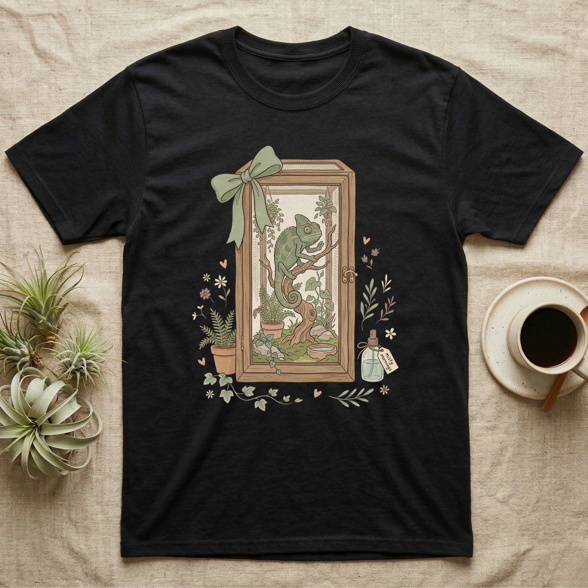 Black t-shirt with a framed illustration of a chameleon, plants, and a potion bottle.