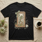 Black t-shirt with a framed illustration of a chameleon, plants, and a potion bottle.