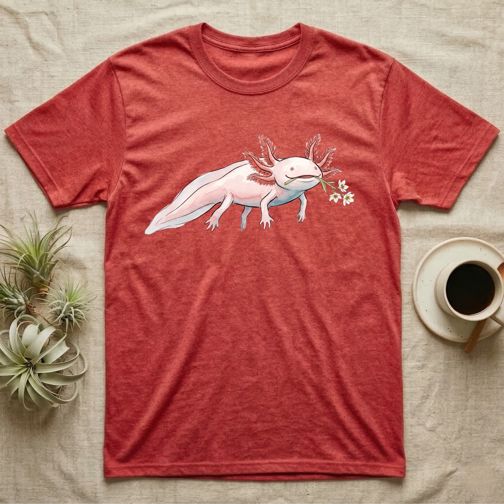 Axolotl Blossom T-Shirt in Heather Red — Watercolor illustration of a pink leucistic axolotl with feathery gills holding an aquatic blossom sprig, on a dark grey t-shirt.