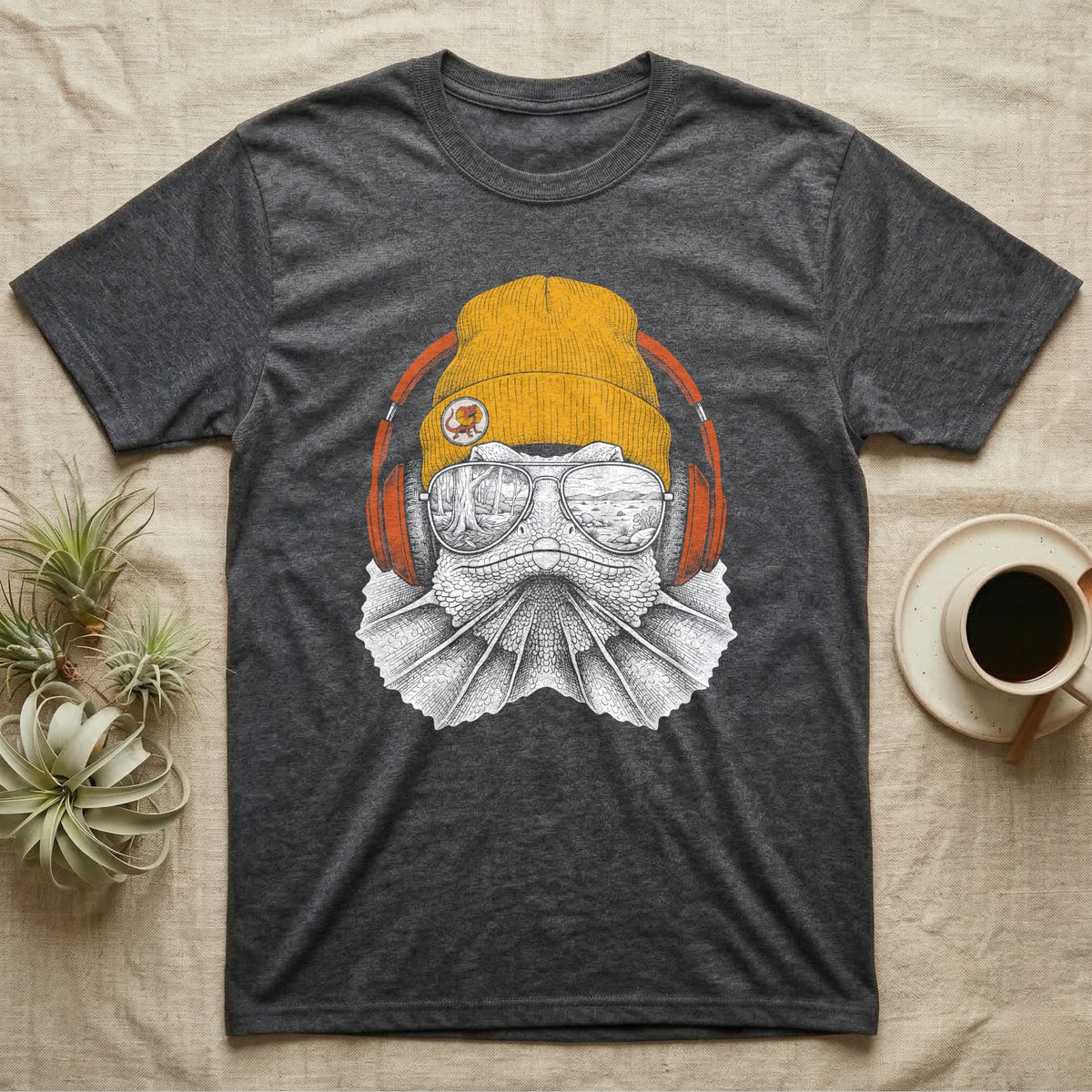 Frilled Lizard Headphones T-Shirt in Dark Heather — Engraved frilled lizard with fanned frill in a beanie and headphones, aviators reflecting savannah woodland.