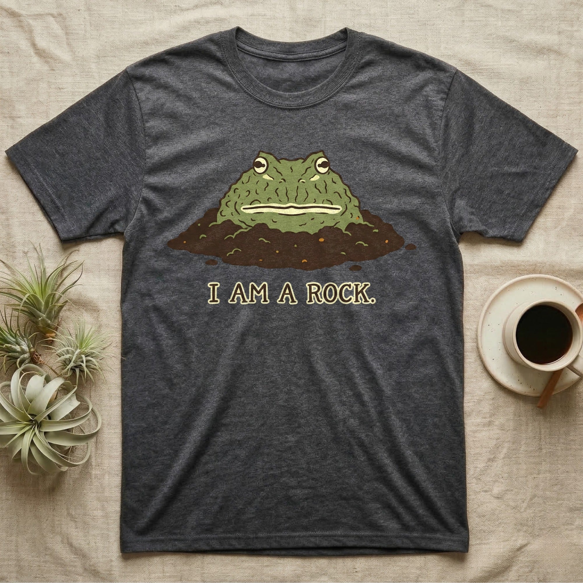 Dark grey t-shirt with a frog emerging from dirt, text reads "I AM A ROCK."