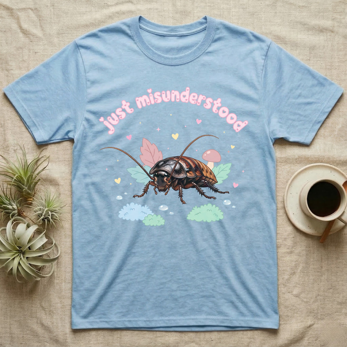Madagascar Hissing Cockroach Baby T-Shirt in Light Blue — Pastel Madagascar hissing cockroach among leaves, mushroom and moss, puffy pink wordmark "just misunderstood" above.