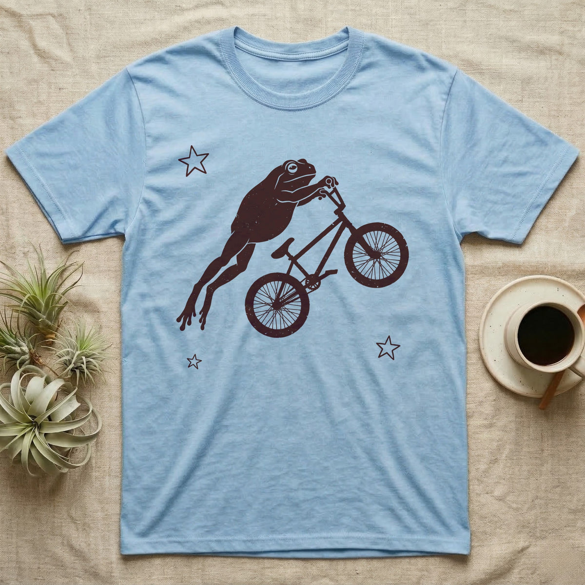 Tree Frog BMX T-Shirt in Light Blue — One-ink worn screen print of a White's tree frog riding a BMX bike mid-air, body stretched straight out behind the handlebars.