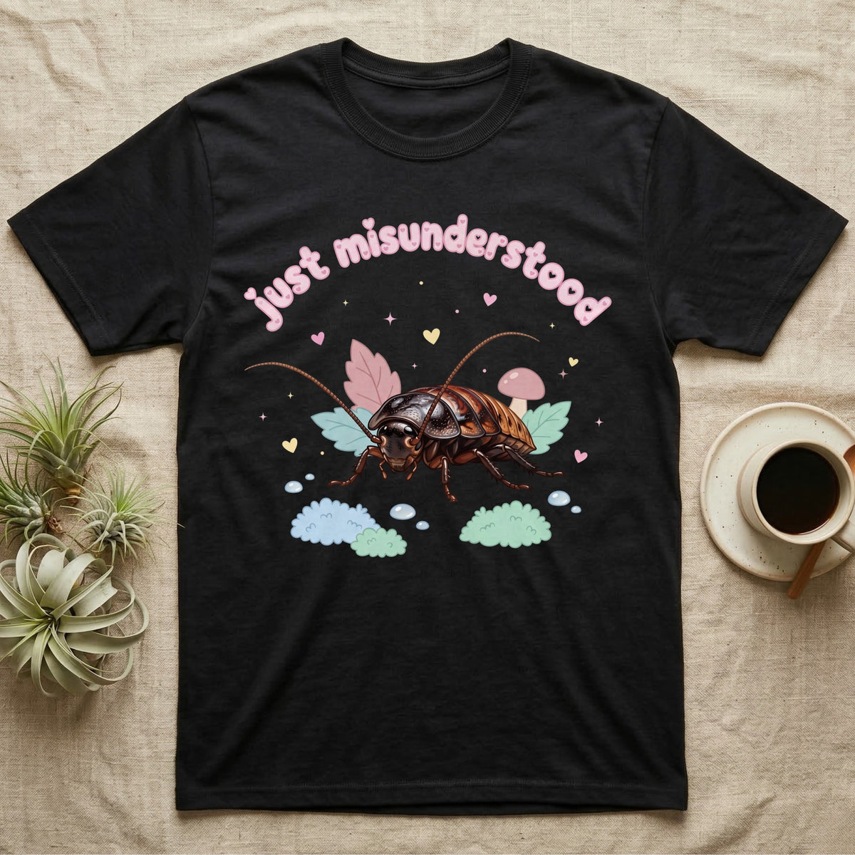 Madagascar Hissing Cockroach Baby T-Shirt in Black — Pastel Madagascar hissing cockroach among leaves, mushroom and moss, puffy pink wordmark "just misunderstood" above.