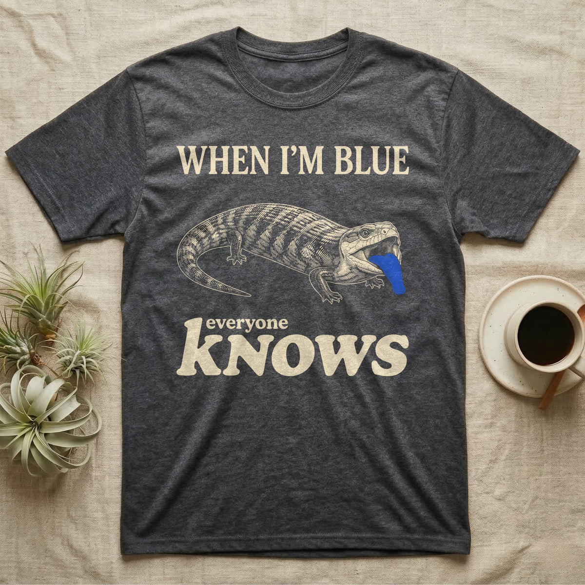 Blue-Tongue Skink Mood T-Shirt in Dark Heather — Cream engraved blue-tongued skink on black flashing a cobalt blue tongue under the words WHEN I'M BLUE everyone KNOWS