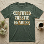 Certified Crestie Enabler T-Shirt in Military Green — Bold retro drop-shadow wordmark reading "Certified Crestie Enabler" in cream and ochre on a grey background.