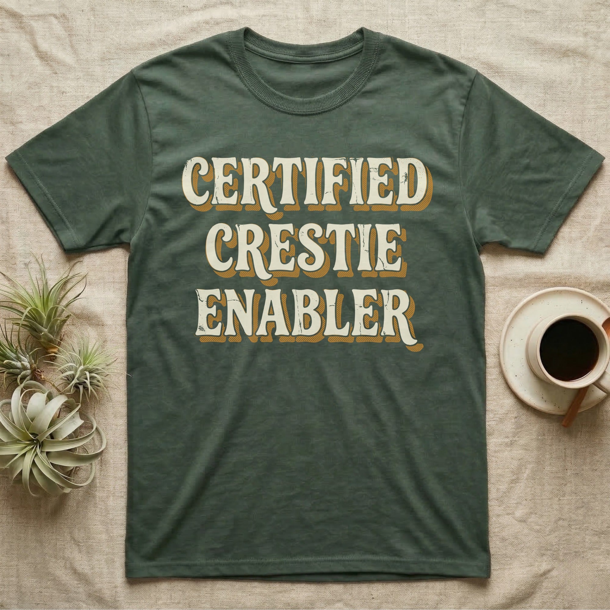 Certified Crestie Enabler T-Shirt in Military Green — Bold retro drop-shadow wordmark reading "Certified Crestie Enabler" in cream and ochre on a grey background.