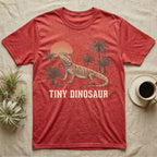 Tiny Dinosaur Bearded Dragon T-Shirt in Heather Red — Retro natural-history illustration of a bearded dragon in profile in a prehistoric landscape with a distressed "Tiny Dinosaur" caption.