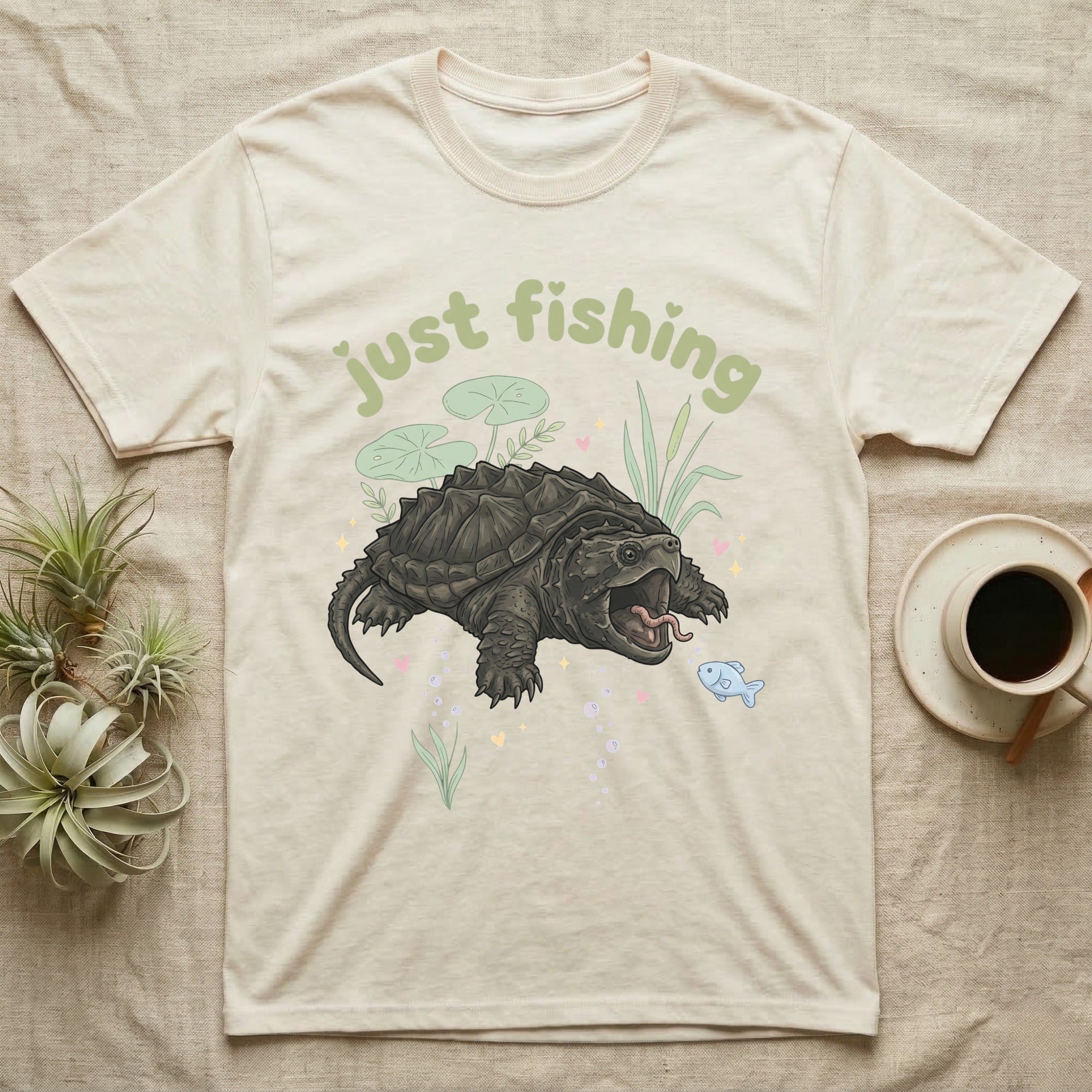 Alligator Snapping Turtle Softie T-Shirt in Natural — Alligator snapping turtle with open mouth and tongue lure under a puffy pastel "just fishing" bubble wordmark.