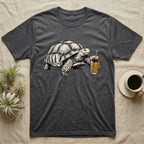 Slow Drip Tortoise T-Shirt in Dark Heather — Flat meme-style illustration of a sulcata tortoise reaching slowly toward a tall iced slow-drip coffee.