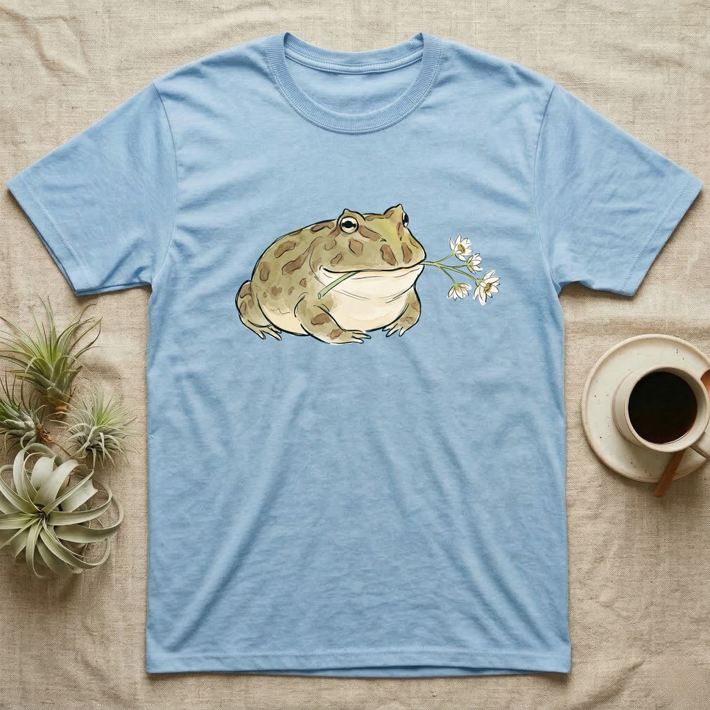 Pacman Frog Blossom T-Shirt in Light Blue — Watercolor illustration of an olive-tan Pacman frog holding a water-lily blossom sprig, on a dark grey t-shirt.