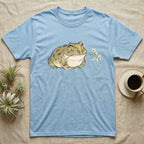 Pacman Frog Blossom T-Shirt in Light Blue — Watercolor illustration of an olive-tan Pacman frog holding a water-lily blossom sprig, on a dark grey t-shirt.